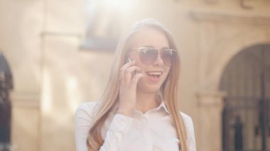 Eski bir şehrin finans bölgesine sokakta yürürken genç çekici iş kadını. Akıllı telefonla konuşuyor