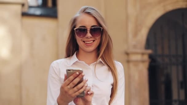 Hermosa mujer de negocios joven con camisa blanca y el uso de teléfono inteligente mientras camina en el centro de la ciudad negocio de Internet de verano fuera de la tecnología ojo primavera móvil cámara lenta calle feliz — Vídeos de Stock