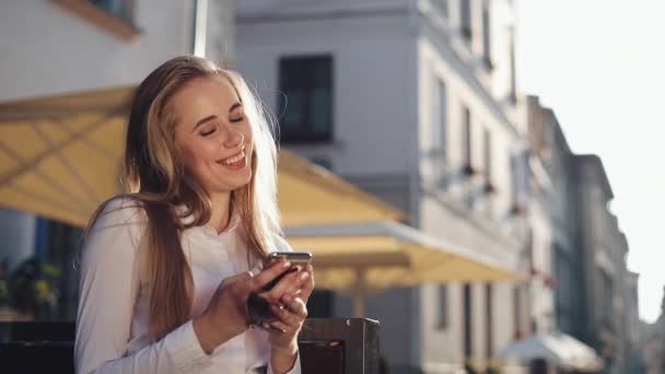 Mulher de negócios atraente sitiing no banco usando smartphone comunicação on-line rede social conectando internet olhando para exibir edifícios da cidade velha no fundo dia ensolarado — Vídeo de Stock