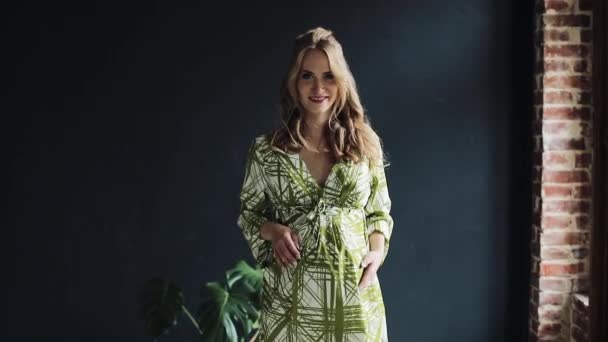 Portrait of pregnant woman at home in green dress. She walking near the window, looking and posing into the camera. Slow motion — Stock Video