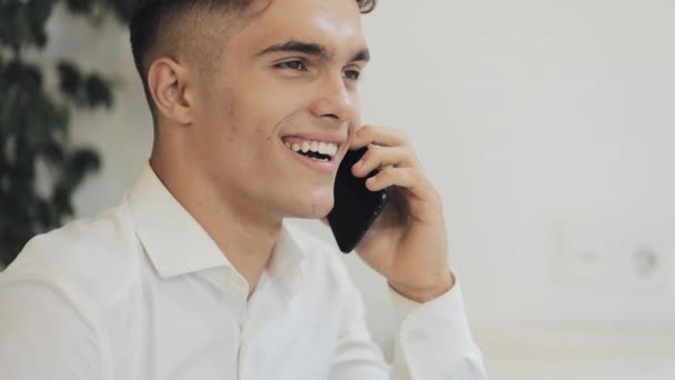 Feliz joven empresario hablando por teléfono móvil en Café cerca de la ventana. Comunicación moderna, tecnologías — Vídeo de stock