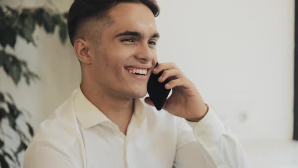 Fröhlicher junger Geschäftsmann, der im Café am Fenster mit dem Handy telefoniert. moderne Kommunikation, Technologien — Stockvideo