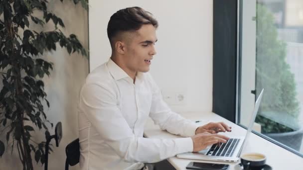Boldog fiatal üzletember működő-ra egy laptop a kávézóban, az ablak mellett. Business, karrier, siker, szabadúszó állás keresés koncepció — Stock videók