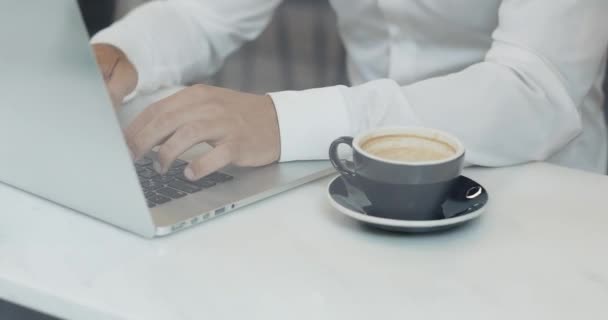 Jonge man met een koffiepauze, hij drinkt koffie en een laptop gebruikt, hand close-up — Stockvideo