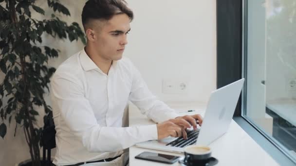 Bonito homem de negócios jovem trabalhando no computador portátil no café. Recebeu boas notícias animadas e felizes. Trabalho independente remoto, estilo de vida moderno ativo de jovens. Conceito de sucesso — Vídeo de Stock