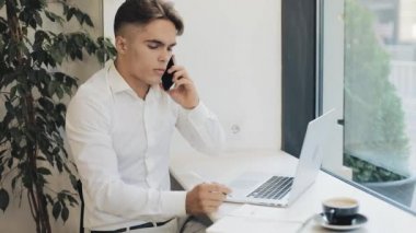 Kahve molası sırasında telefonla konuşurken not defterinde notlar alarak konsantre genç işadamı orta çekim