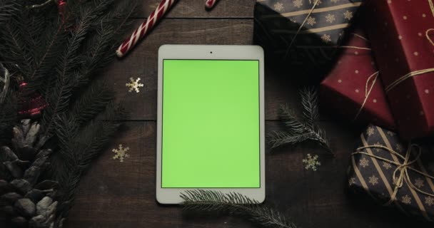 Вид сверху. Белый планшетный аппарат с зеленым экраном на старом деревянном столе с рождественским украшением. Хрома-ключ. Вертикальное положение. Новогодняя концепция — стоковое видео