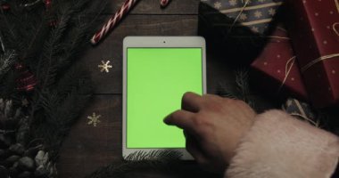 Claus Santa yeşil ekran beyaz tablet bilgisayarınızla sayfalarında dokunarak eller. Chroma anahtar. Üstten görünüm. Dikey konum. Yılbaşı yeni yıl kavramı