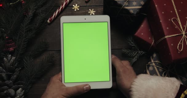 Руки Санта-Клауса держат белый планшетный компьютер с зеленым экраном. Хрома-ключ. Вид сверху. Вертикальное положение. Новогодняя концепция — стоковое видео