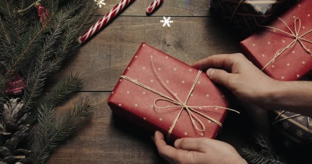 Male hands put give big New year present on style wooden background with New year decoration and Xmas tree with blurred blinking lights — Stock Video