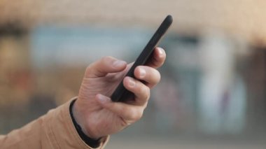 Elleri shopping mall yakınındaki sokakta smartphone kullanan genç adam. İletişim, online alışveriş, sohbet, sosyal ağ kavramı. Yakın çekim