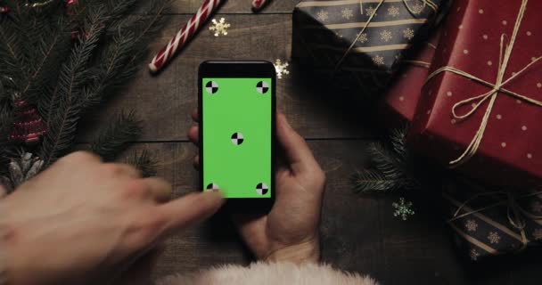 Rukou Santa Claus výčepní stránky na černé smartphone s zeleným plátnem. Chromatický klíč. Pohled shora. Svislá pozice. Koncept Vánoce Nový rok — Stock video