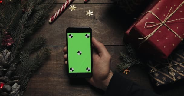 Tangan pria memegang smartphone hitam dengan layar hijau. Tangan lain menempatkan beberapa kotak hadir di atas meja. Kunci Chroma. Pemandangan bagus. Konsep pemesanan internet Tahun Baru Natal — Stok Video