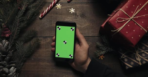 남자 손 잡고 녹색 화면 블랙 스마트폰입니다. 다른 손은 테이블에 몇 가지 있는 상자를 배치. 크로마 키입니다. 최고의 볼 수 있습니다. 크리스마스 새 해 인터넷 주문 개념 — 비디오