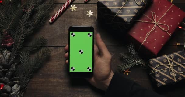 Mani maschili che tengono lo smartphone nero con schermo verde. Altre mani posizionare alcune scatole presenti sul tavolo. Chiave cromatica. Vista dall'alto. Natale Capodanno concetto di ordine internet — Video Stock