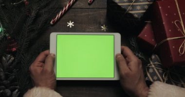 Noel Baba ile yeşil perde beyaz tablet bilgisayarda sayfaları tutan eller. Chroma anahtar. Üstten görünüm. Yatay konum. Yılbaşı yeni yıl kavramı