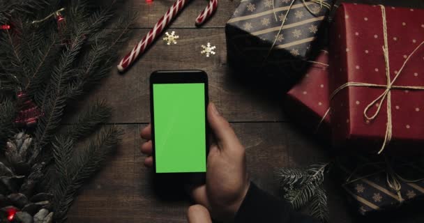 Mains masculines défilant, tapotant, zoomant pages sur le smartphone noir avec écran vert. Clé chromatique. Vue de dessus. Position verticale. Noël Nouvel An concept — Video