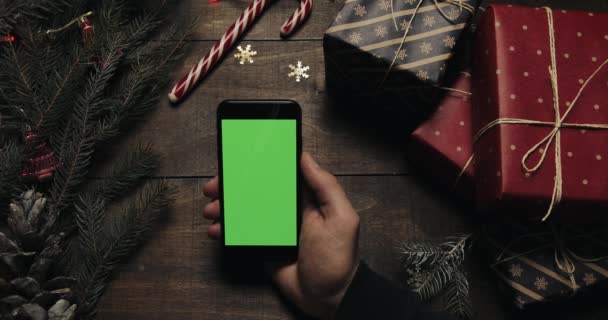 Mains masculines défilant, tapotant, zoomant pages sur le smartphone noir avec écran vert. Clé chromatique. Vue de dessus. Position verticale. Noël Nouvel An concept — Video