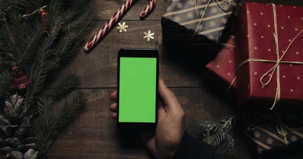 Mãos masculinas segurando smartphone preto com tela verde. Outras mãos colocando algumas caixas de presente sobre a mesa. Chave Chroma. Vista superior. Natal Ano Novo conceito de ordem de internet — Vídeo de Stock