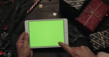 Eller kaydırma, dokunarak, yeşil ekran ile beyaz tablet bilgisayarda sayfa yakınlaştırma Claus Santa. Bazı mevcut kutuları masaya yerleştirerek başka eller.