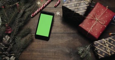 Üstten görünüm. Siyah smartphone ile yeşil perde Noel tatil dekorasyonu ile masanın üzerinde yatan. Noel Baba'nın ellerini bir hediye masaya koyar. Noel tatil dekorasyon üstten görünüm kavramı