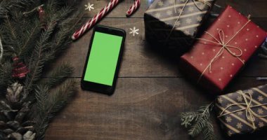 Üstten görünüm. Siyah smartphone ile yeşil perde Noel tatil dekorasyonu ile masanın üzerinde yatan. Noel Baba'nın ellerini bir hediye masaya koyar. Noel tatil dekorasyon üstten görünüm kavramı