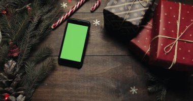 Üstten görünüm. Siyah smartphone ile yeşil perde Noel tatil dekorasyonu ile masanın üzerinde yatan. Erkek ellerini bir hediye masaya koyar. Noel tatil dekorasyon üstten görünüm kavramı. Ahşap arka plan