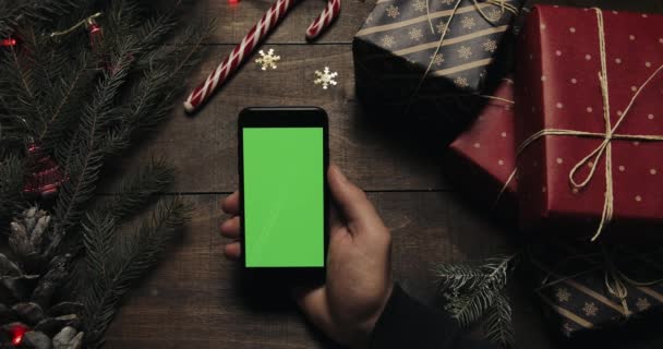 Mãos masculinas tocando páginas no smartphone preto com tela verde. Chave Chroma. Vista superior. Posição vertical. Conceito de Natal Ano Novo — Vídeo de Stock