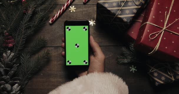 Mãos de Papai Noel segurando smartphone preto com tela verde. Chave Chroma. Vista superior. Posição vertical. Conceito de Natal Ano Novo — Vídeo de Stock