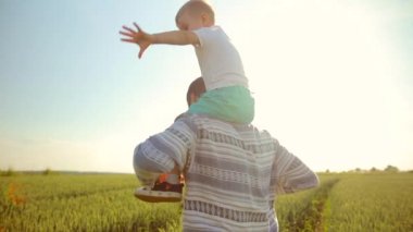 Baba oğlu onun omuzlarında giyer. Gün batımı sırasında buğday alan üzerine bir yürüyüş. Babalar günü Aile kavramı