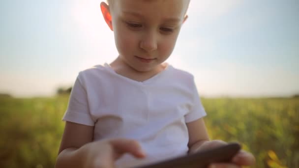 Malý chlapec stojí uprostřed pole, používá smartphone, někdo hraje hry, publikuje fotografie. Zábavné, moderní děti na internetu — Stock video