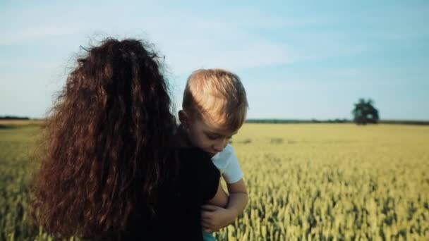 La madre porta suo figlio sulle spalle. Una passeggiata sul campo di grano durante il tramonto. Festa della mamma Concetto di famiglia — Video Stock