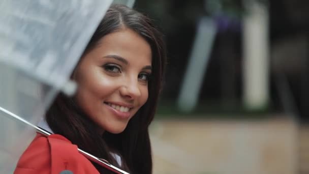 Retrato de una mujer sonriente bajo un paraguas en la ciudad mirando a la cámara. Primavera u otoño — Vídeo de stock