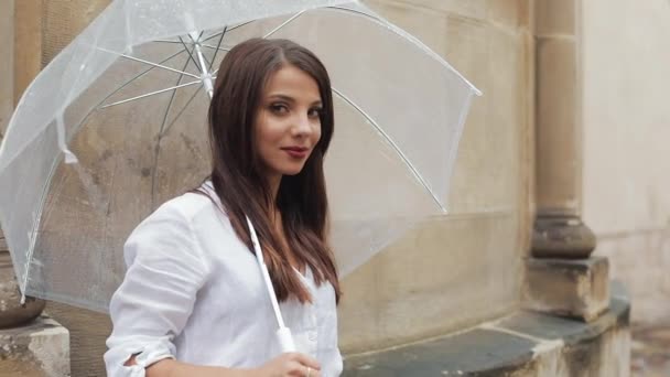 Retrato de jovem mulher sorrindo fica com guarda-chuva na mão na rua e olhando para a câmera — Vídeo de Stock