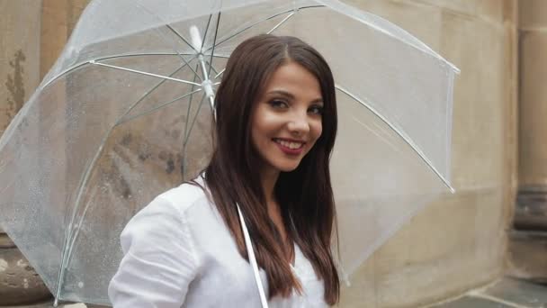 Ritratto di giovane donna sorridente in piedi con l'ombrello in mano per strada e guardando nella fotocamera — Video Stock