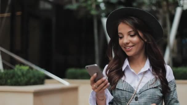 Профессиональная молодая деловая женщина ходит по городской улице с помощью смартфона. Концепция: новый бизнес, коммуникация, банкир. Снаружи, медленная съемка — стоковое видео