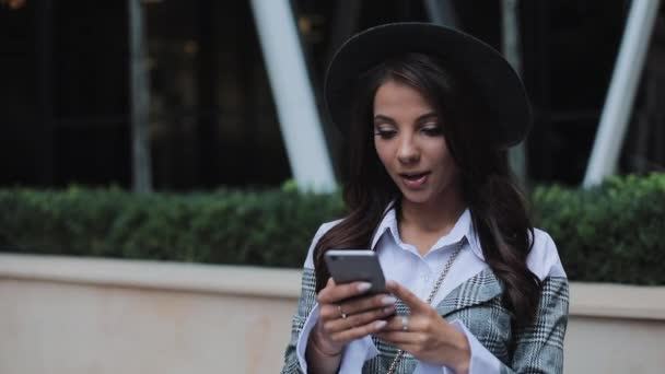 Joven empresaria profesional parada en la calle urbana y usando un teléfono inteligente. Está mirando a la cámara. Concepto: nuevo negocio, comunicación, banquero. Afuera, cámara lenta — Vídeos de Stock