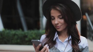 Kentsel Caddesi üzerinde duran ve smartphone kullanarak profesyonel genç iş kadını. Kameraya bakıyor. Konsept: yeni iş, iletişim, bankacı. Dış, ağır çekim