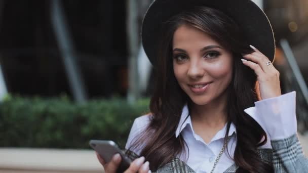 Jeune femme d'affaires professionnelle debout sur la rue urbaine et utilisant un smartphone. Elle regarde dans la caméra. Concept : nouvelle entreprise, communication, banquier. Dehors, au ralenti — Video