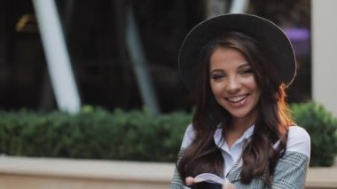 Kentsel Caddesi üzerinde duran ve smartphone kullanarak profesyonel genç iş kadını. O kameraya bakıyor ve gülümsüyor. Konsept: yeni iş, iletişim, bankacı. Dış, ağır çekim