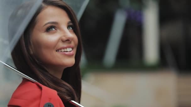 Retrato de una mujer sonriente bajo un paraguas en la ciudad mirando hacia los lados. Está parada en la calle cerca del centro de negocios. De cerca. Primavera u otoño — Vídeo de stock