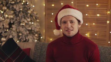 Noel Baba şapkası kameraya Noel ağacı özgeçmişlerine bakarak güleryüzlü çekici adam portresi. Ağır çekim
