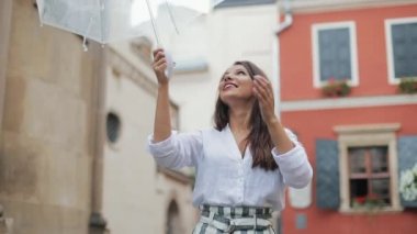 # Gökyüzünü arayan ve yağmur durdurursanız kontrol etmek için el yükselterek yakışıklı genç iş kadını. O gülümseyen ve onun şemsiye yağmur sonu zevk kapatın