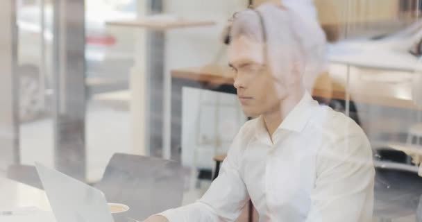 En allvarlig ung affärsman sitter vid ett bord på ett café som arbetar på en bärbar dator. Frilans, kommunikation, It, framgångsrika människor — Stockvideo