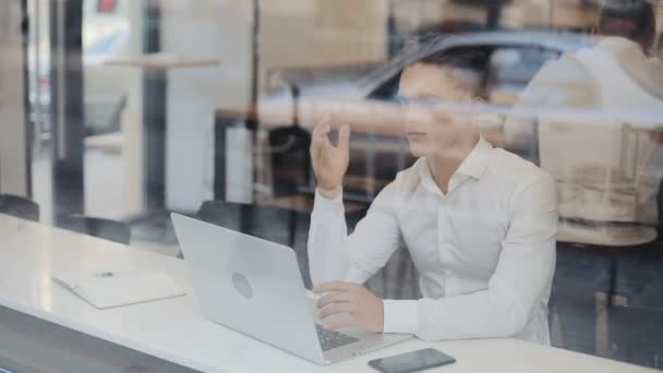 Cansado jovem empresário sentado em uma mesa em um café trabalhando em um laptop. Freelance, comunicação, TI, conceito de empresário cansado — Vídeo de Stock