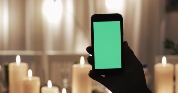 Mão masculina está segurando Smartphone com tela verde. Velas iluminadas no fundo — Vídeo de Stock