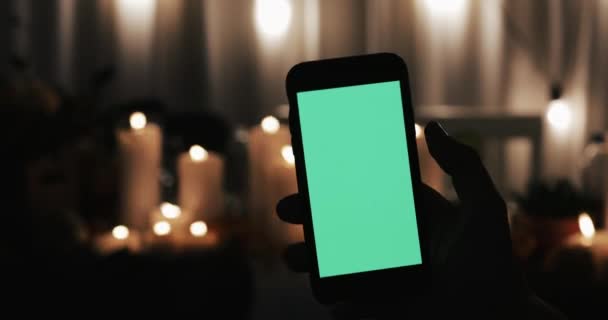 雄手持有智能手机与绿色屏幕 几种类型的运动 向右滑动和点击 背景中的灯火通明的蜡烛 — 图库视频影像