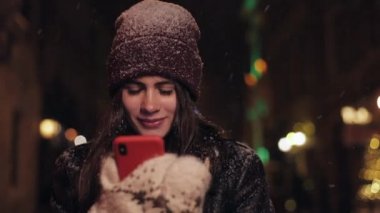 Geceleri şehir street yürüyüş smartphone ile genç kadın portresi. App akıllı şehir geceleri kullanan kadın. Kar düşüyor. Bulanık gece