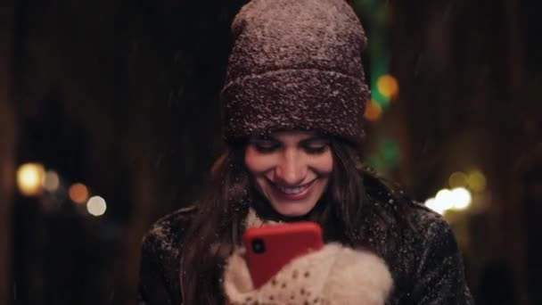 Portrét mladé ženy s smartphone pěší ulici v noci. Žena pomocí aplikace na chytrém telefonu ve městě v noci. Sníh padá. Rozmazané noc — Stock video