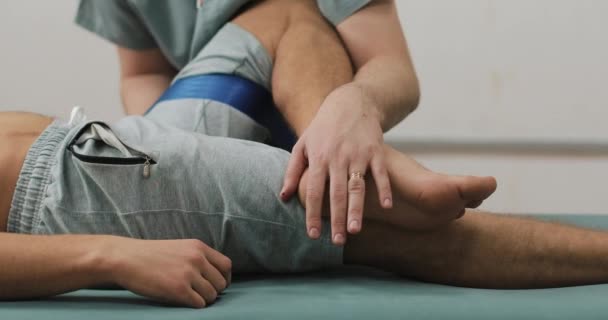 Фізіотерапевт, який працює з пацієнтом чоловічої статі. Він розтягує пацієнта на ліжку в лікарні — стокове відео